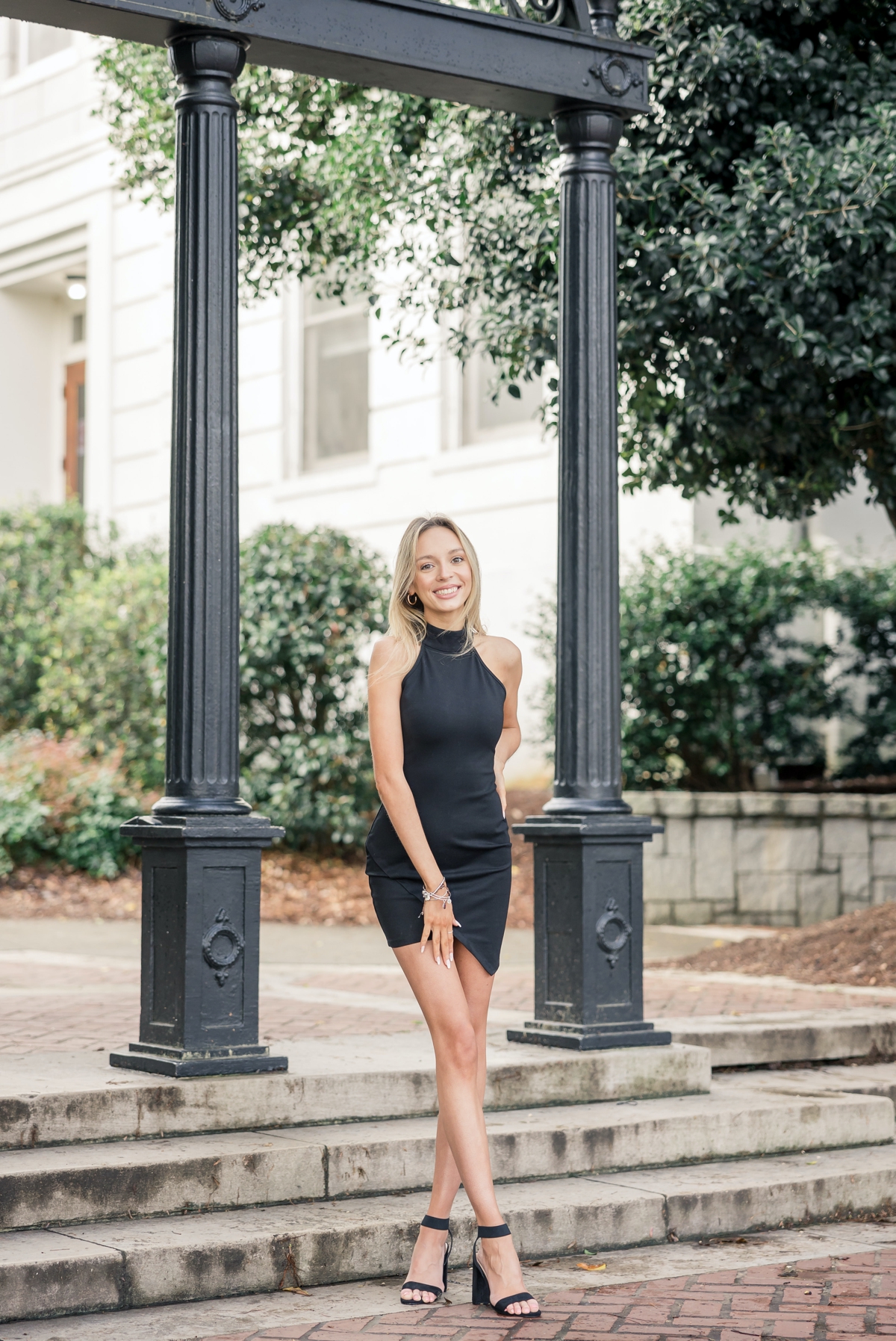 Woman standing at the entrance to UGA's campus with her legs elegantly crossed smiling