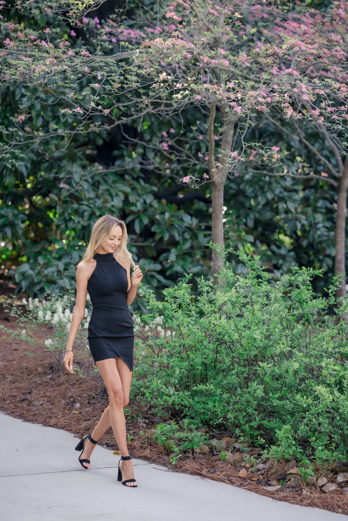 UGA graduate walks through a garden on campus playing and looking down at her hair