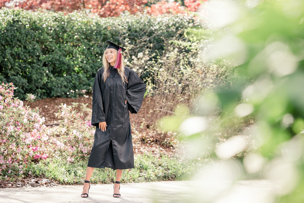 A look at a woman smiling off in the distance in her college graduation cap and gown through the branches of a tree on UGA's campus.