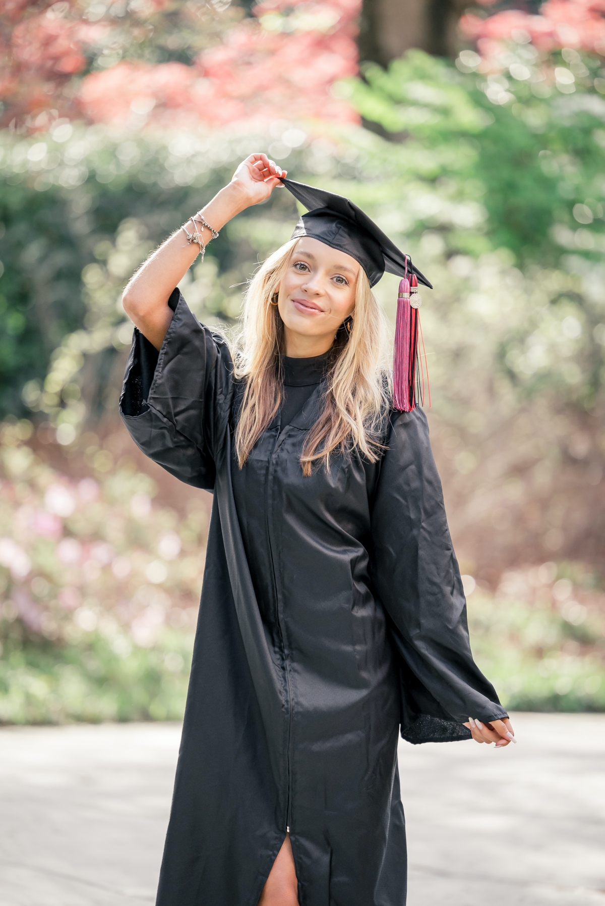 Woman holding her cap on her head with one hand as she smiles during her college graduation photos