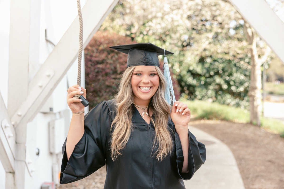A UGA graduate holding the graduation bell cord while she touches the tassel on her cap.
