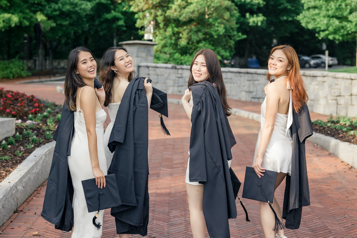 Four college seniors walking across campus with their cap and gowns thrown over their shoulders.