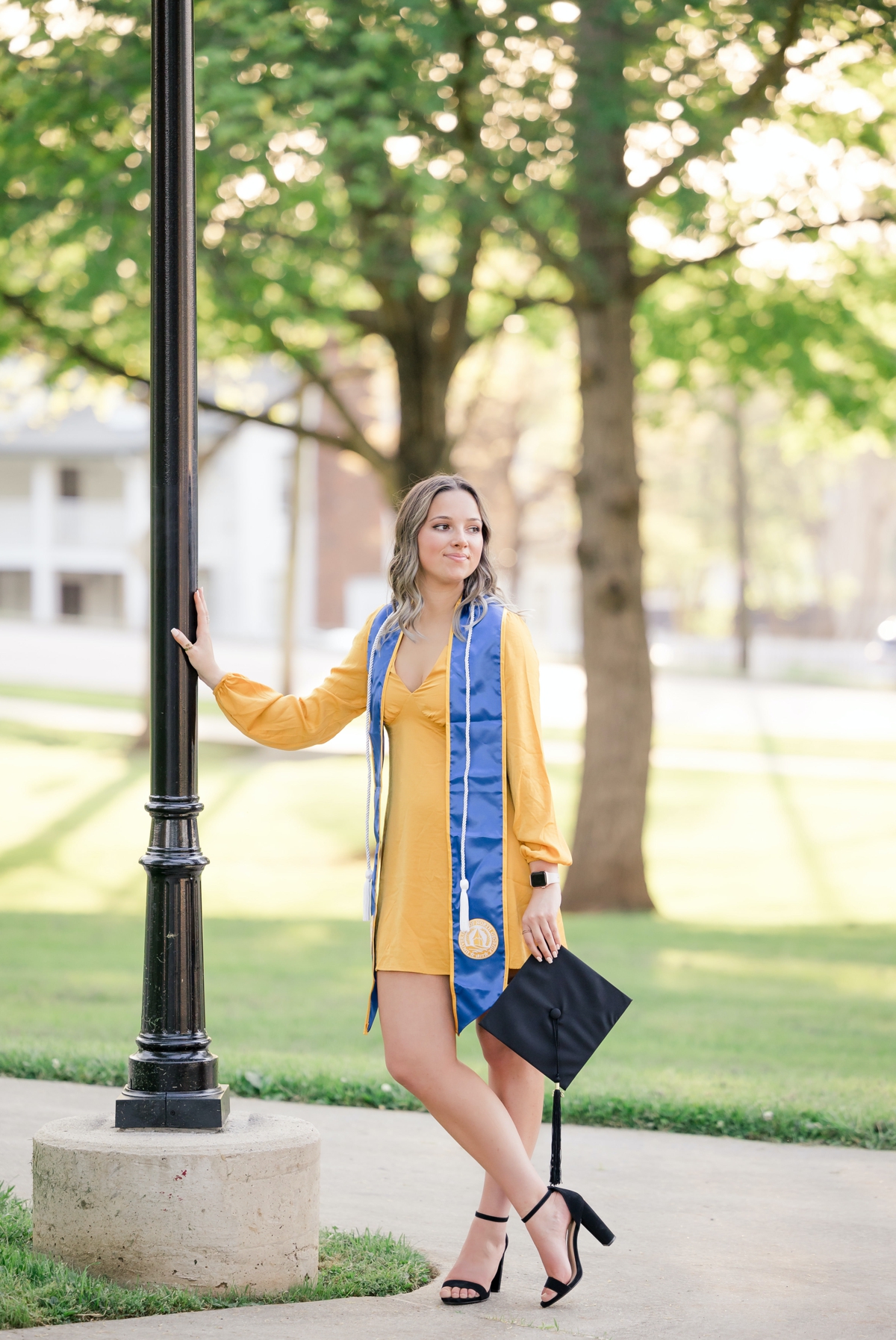 A woman in a yellow dress leaning against a lamp post during her graduation session.