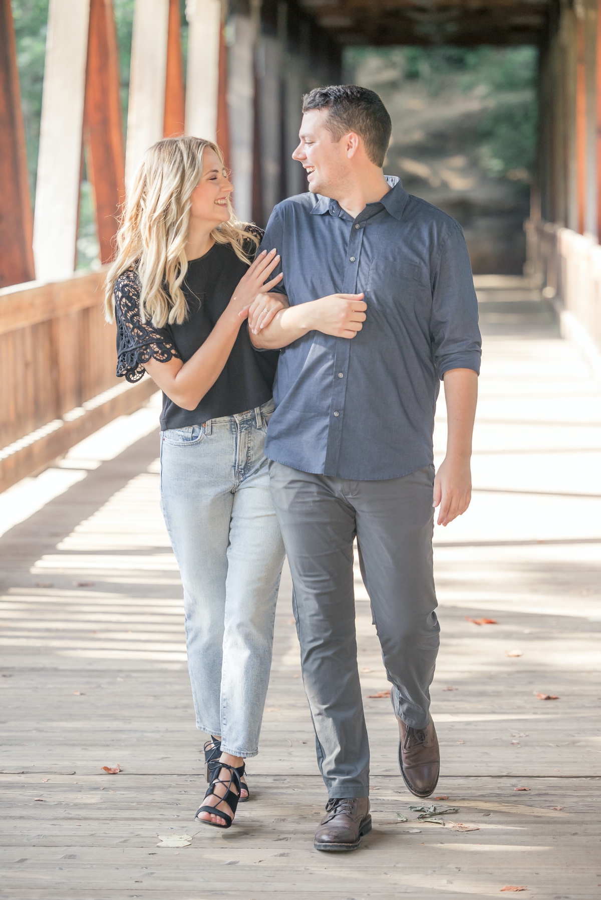 Julia holding Taylor's arm while they walk together across a bridge during their engagement session with Five Fourteen Photography.