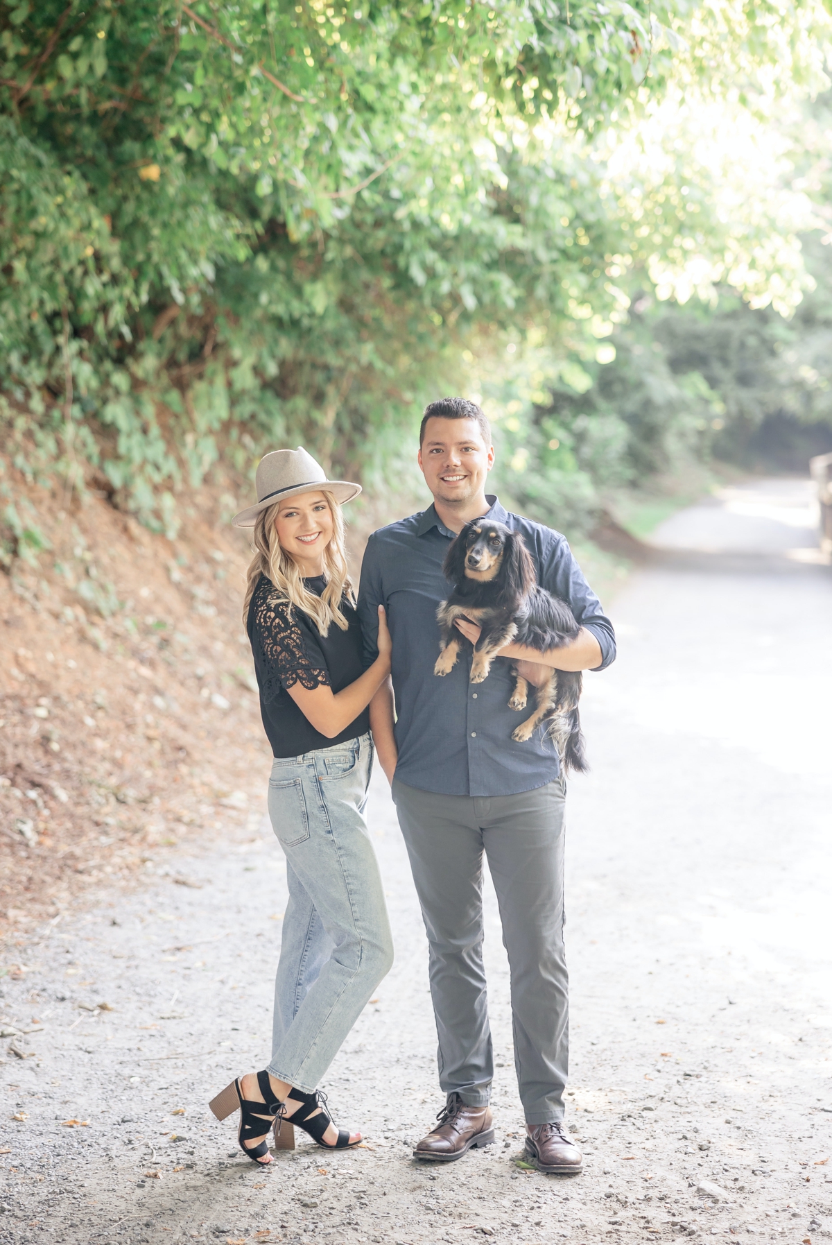 Julia and Taylor holding their dog on a path during their engagement session.
