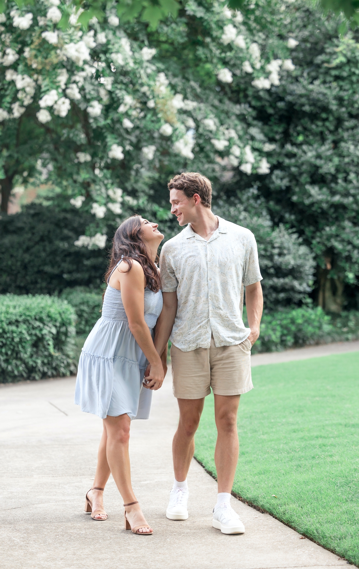 Brooke holding Isaac's hand while she laughs up at him as they walk through Piedmont Park during their portrait session.