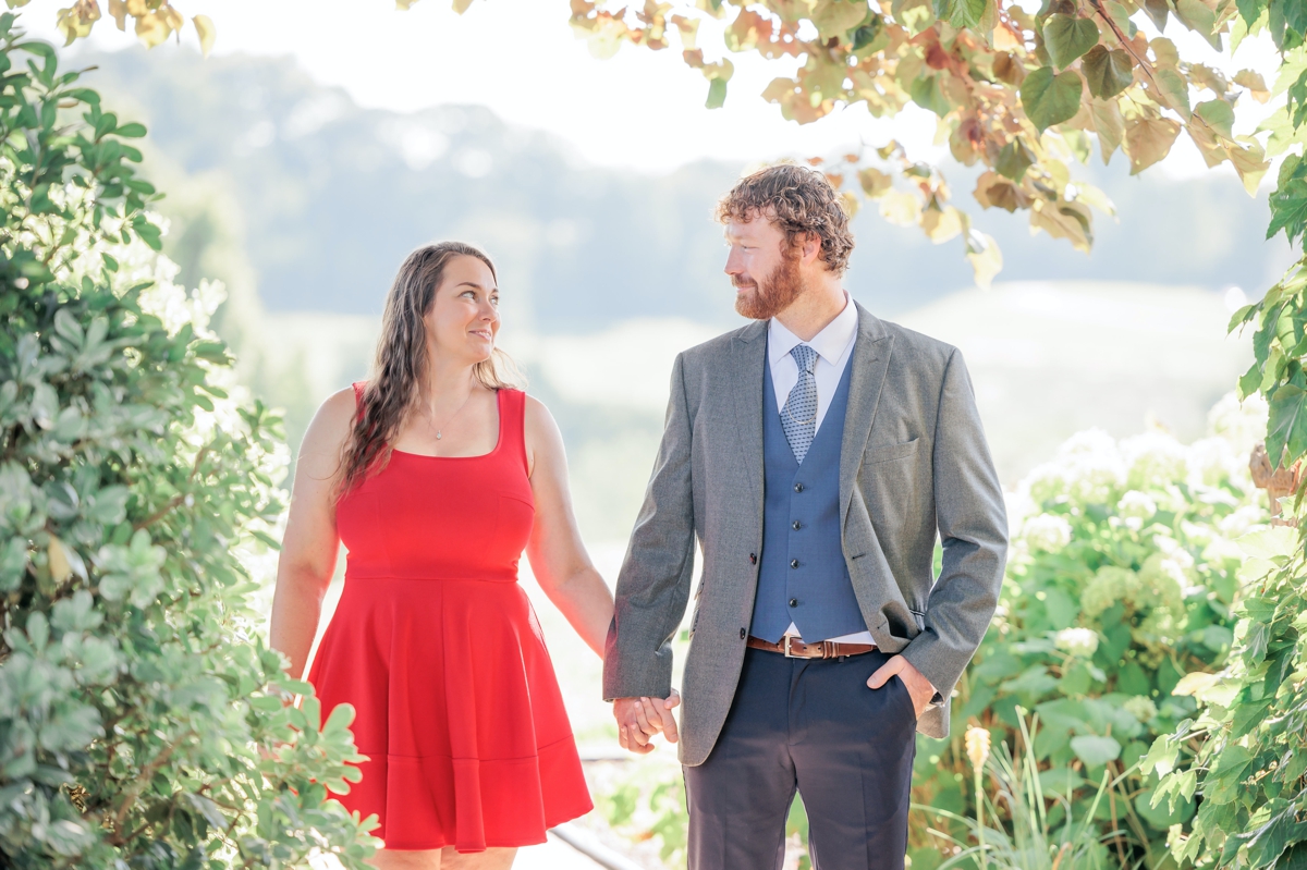 Rachel and Matthew standing in a garden holding hands and smiling at each other during their engagement session.