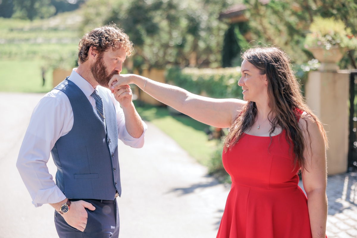 Matthew kissing Rachel's hand while she smiles during their winery engagement session.