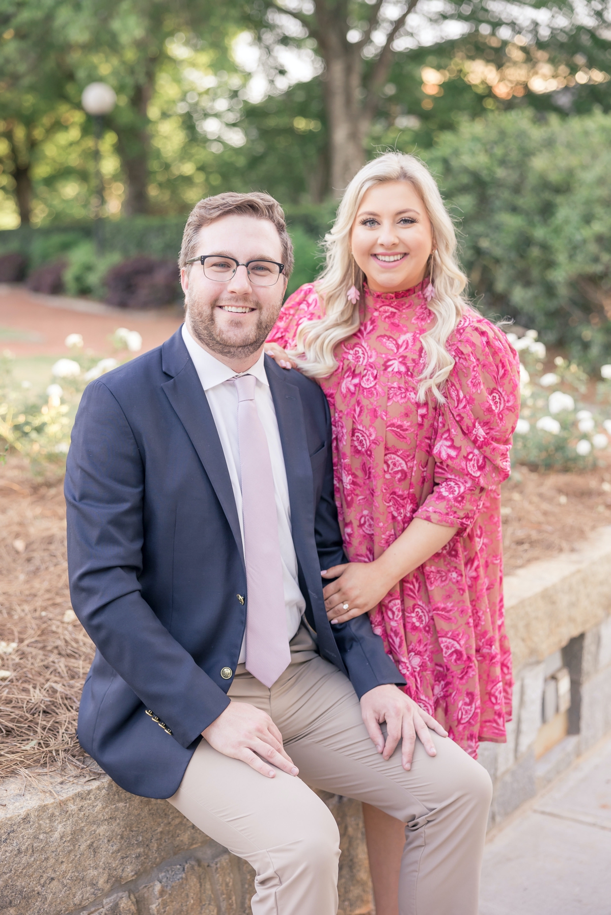 Austin and Sydney sitting on the edge of a bridge smiling during their Atlanta Athletic Club engagement session.