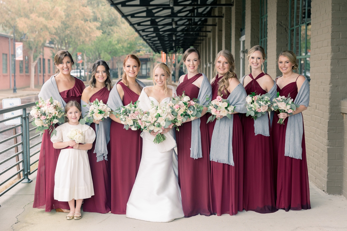 Rebecca smiling with her bridesmaids in burgundy gowns on her wedding day.