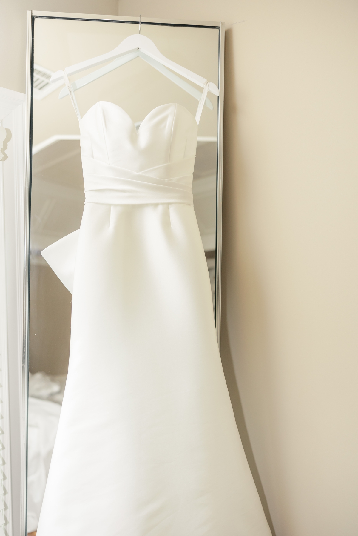 Detail photo of the bride's satin wedding gown hanging on a mirror. 