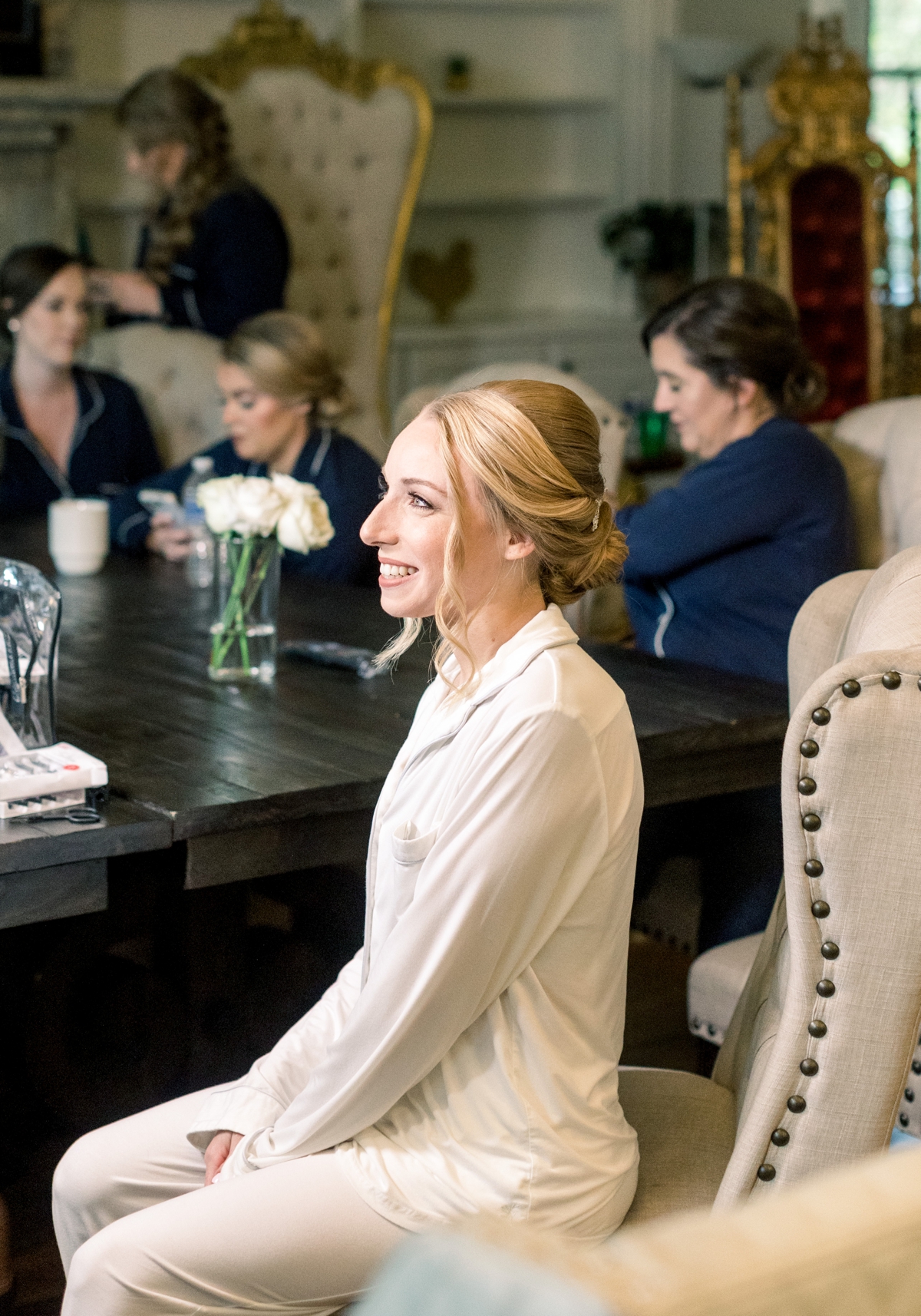 Rebecca smiling as she sits in a chair talking with her bridesmaids on her wedding day at Foundry Puritan Mill.