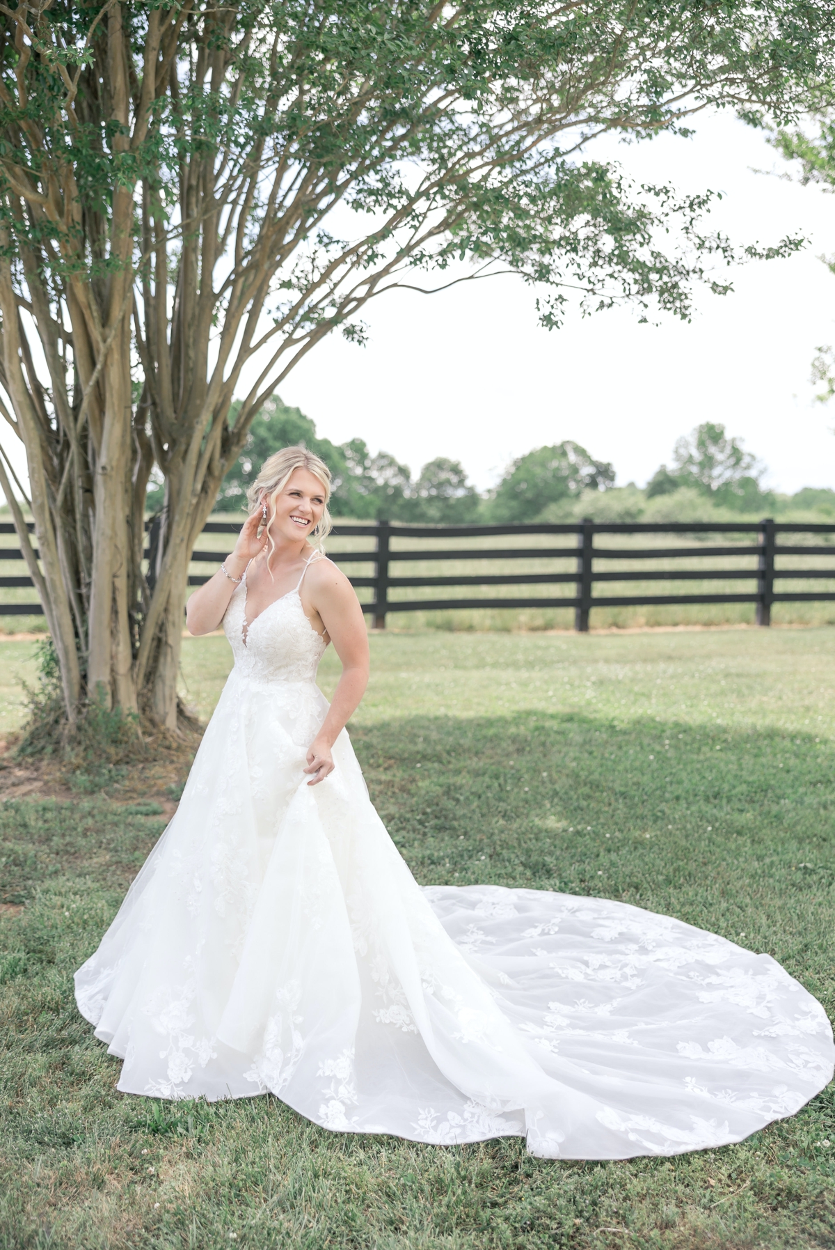 Grace playing with her hair and laughing over her shoulder as she stands by a tree on the lawn of Walters Barn in Lula GA in her wedding gown.