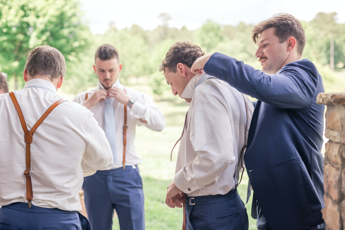 Chris and his groomsmen helping each other into their wedding day suits in front of the groom's suit at Walters Barn.