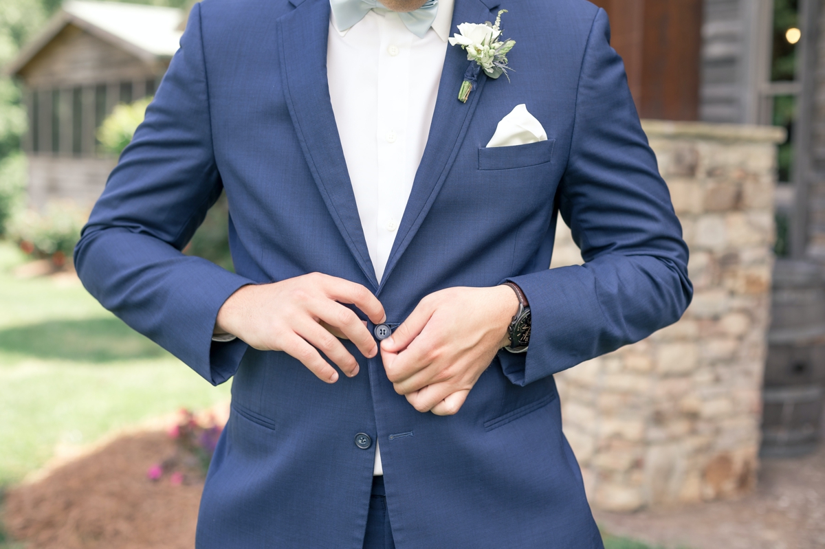 Detail photo of Chris buttoning his blue wedding suit.