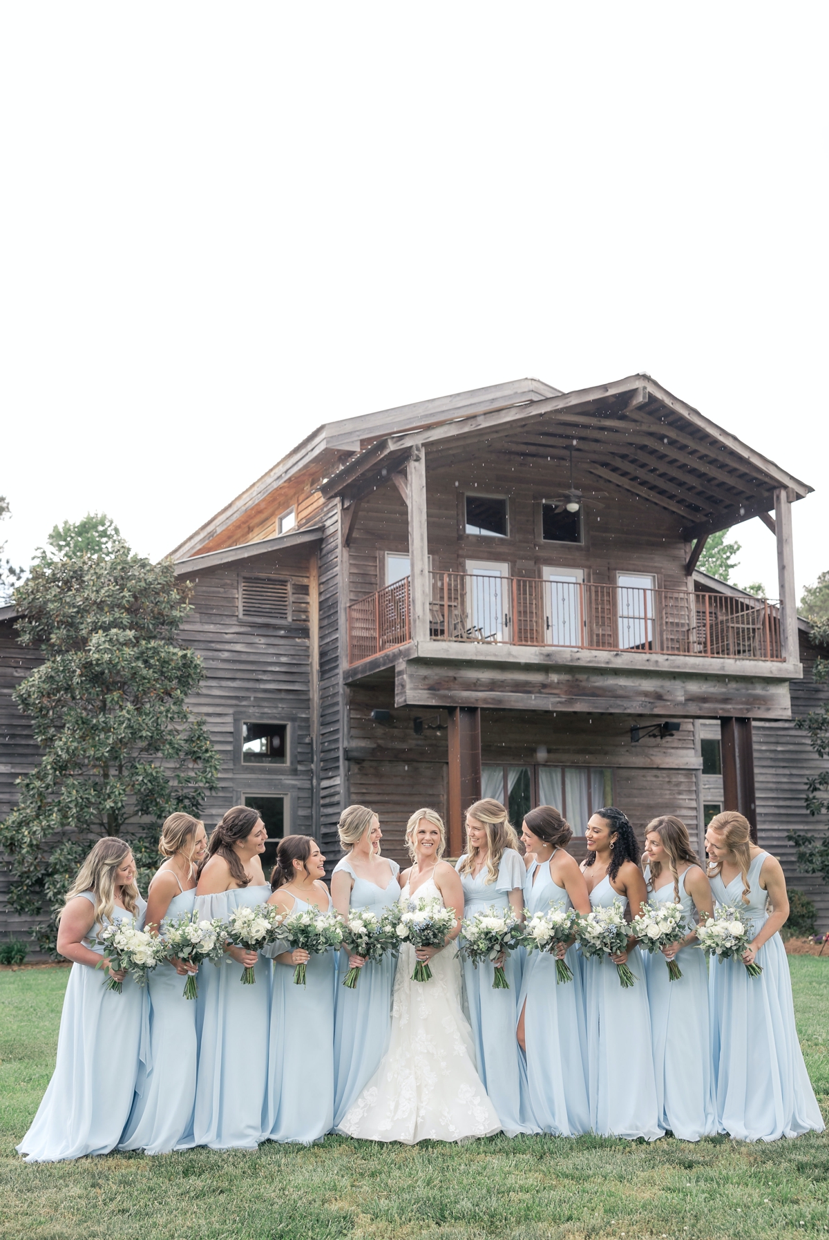 Grace and her bridesmaids smiling at each other in front of Walters Barn on her wedding day.