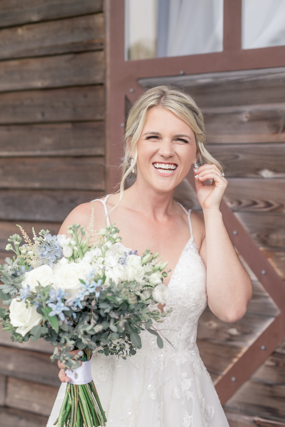 Grace smiling and laughing as she lightly touches her earring on her wedding day.