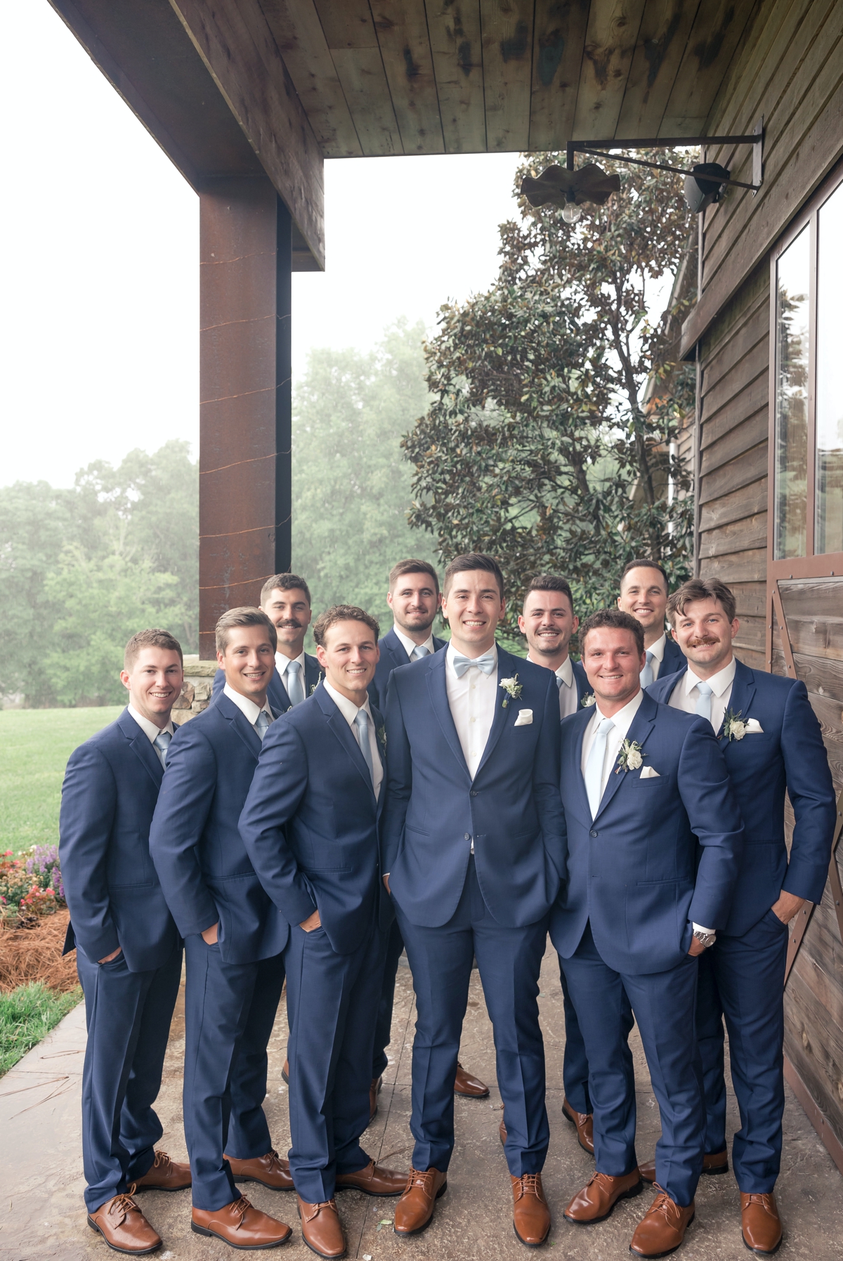 Chris and his groomsmen in their blue wedding day suits smiling under the porch overhanging of Walters Barn in Lula GA on his wedding day.