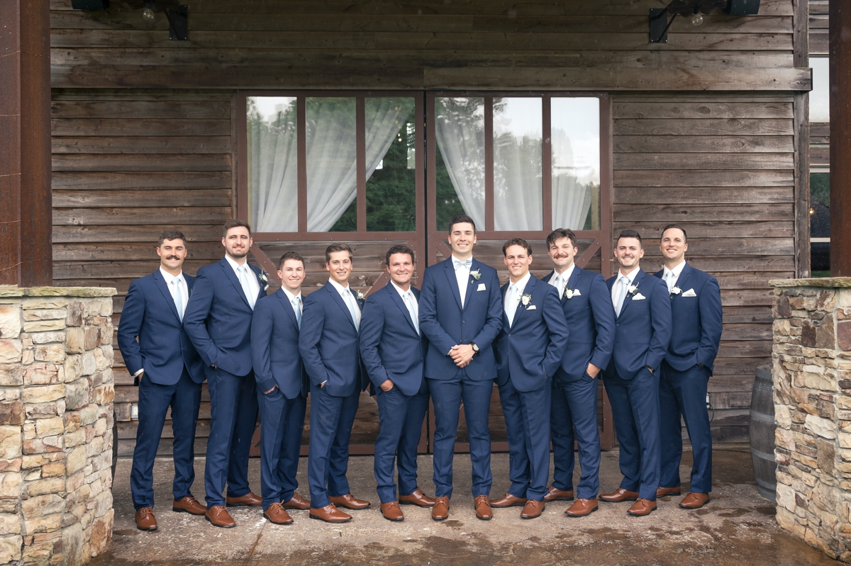 Chris smiling with his groomsmen on his wedding day in front of Walters Barn.