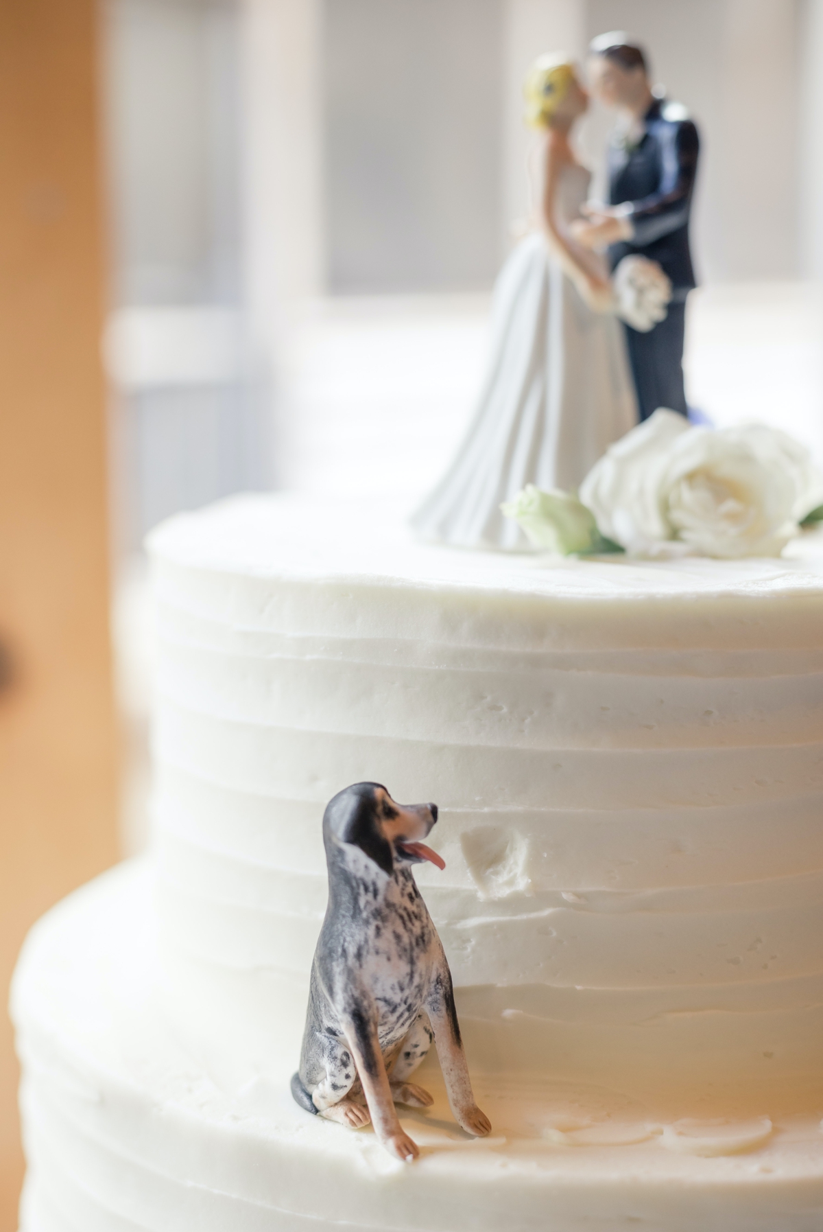 Detail photo of a dog figurine taking a bit out of the wedding cake and the cake topper of the bride and groom kissing for Chris and Grace's wedding day.