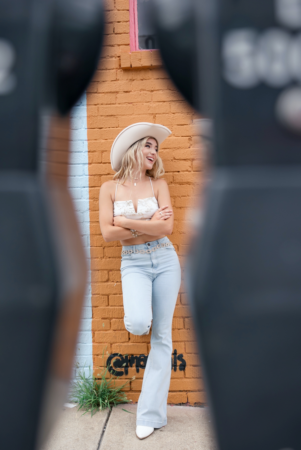 A blonde senior girl leaning against a wall shown through parking meters during her senior session. 