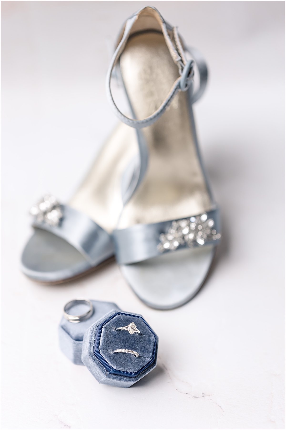 bridal detail photo of blue sandal wedding shoes with rhinestones on them and the wedding rings in a matching blue ring box 