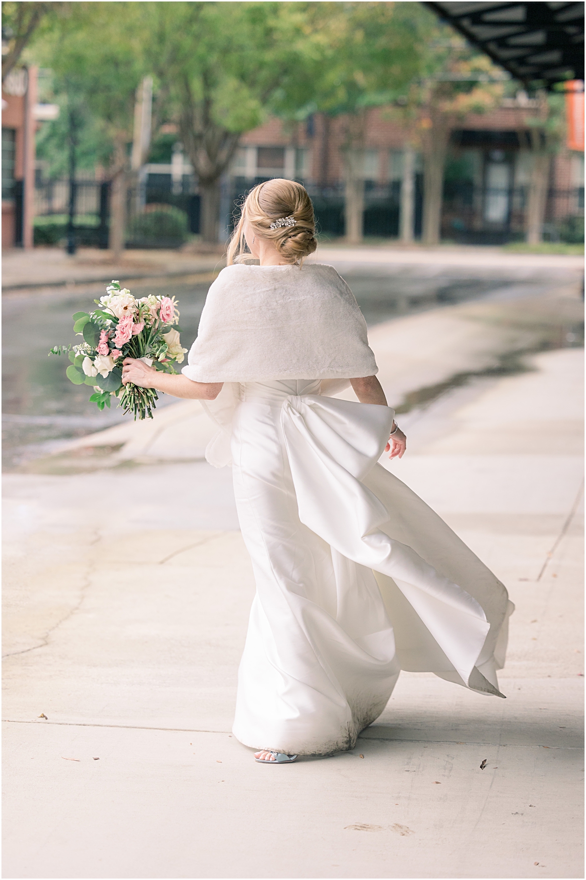 view of the back of Rebecca's elegant wedding dress with a big white bow and white fur cape as she walks away