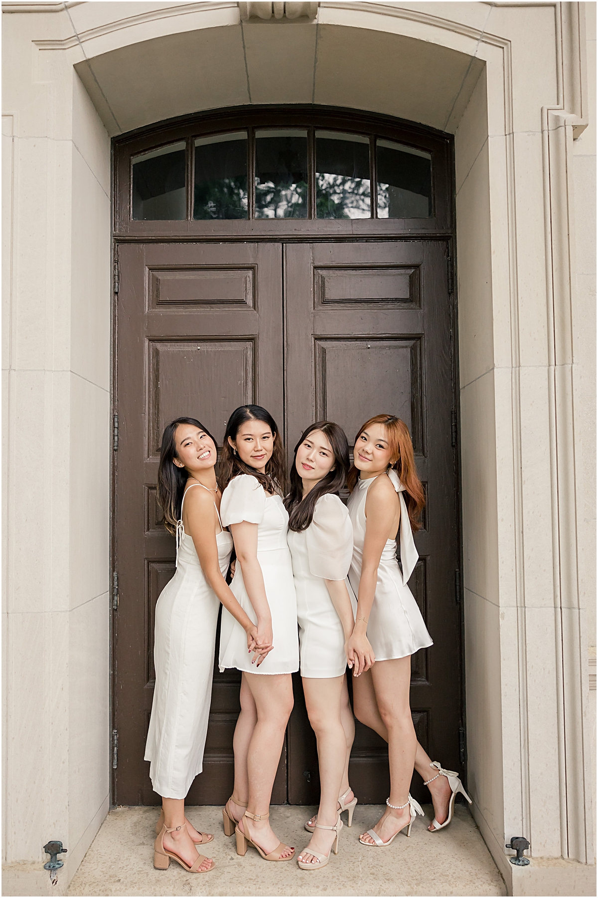 4 girls at Emory University in different styles of white dresses posing in front of brown doors for an Emory University Senior Photographer