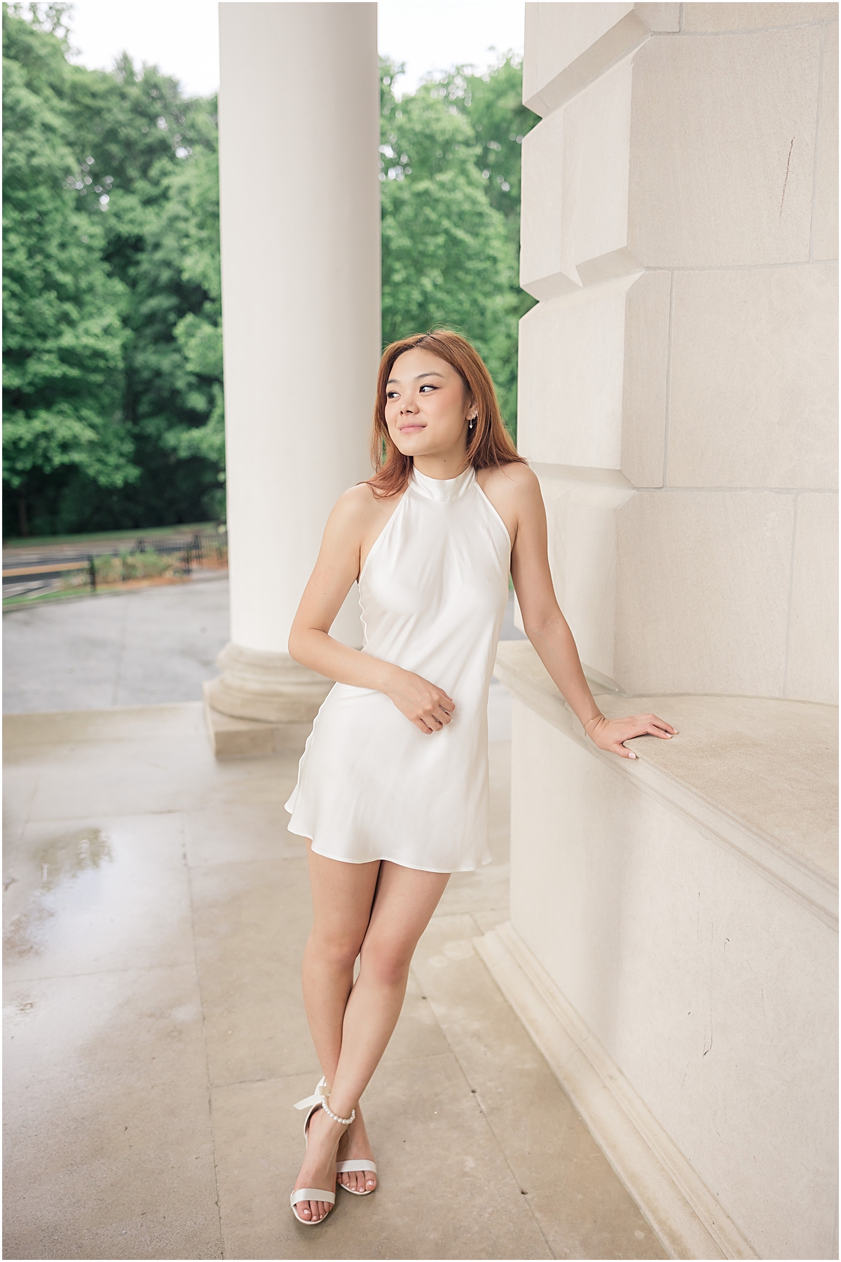 female graduate with red hair leaning against white ledge of building while looking past the Emory University Senior Photographer