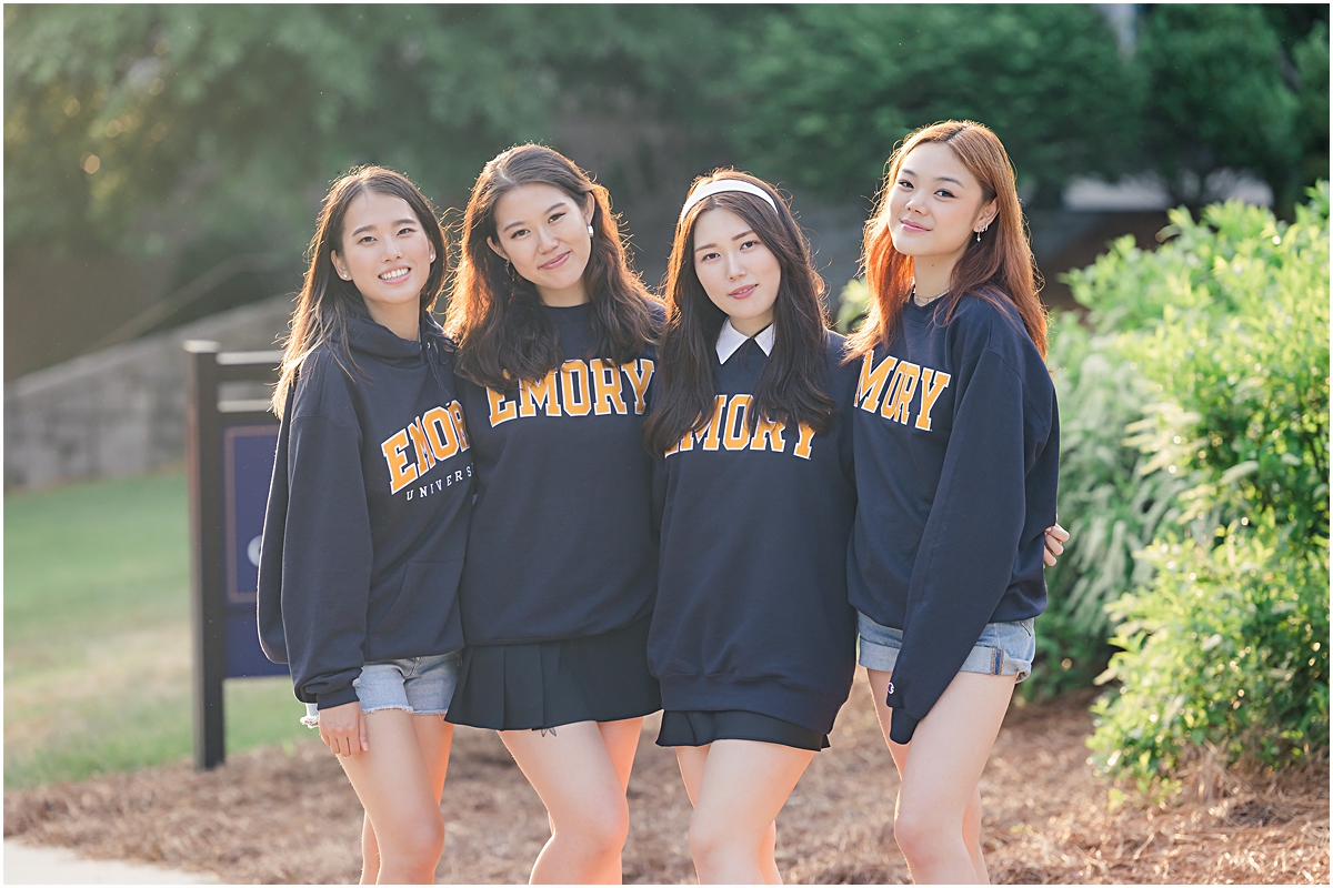 4 female graduates of Emory University in GA standing with their arms around each other wearing matching navy blue long sleeve t-shirts that say "Emory" in block letters in gold with white outlines as they pose for a picture for the Emory University Senior Photographer